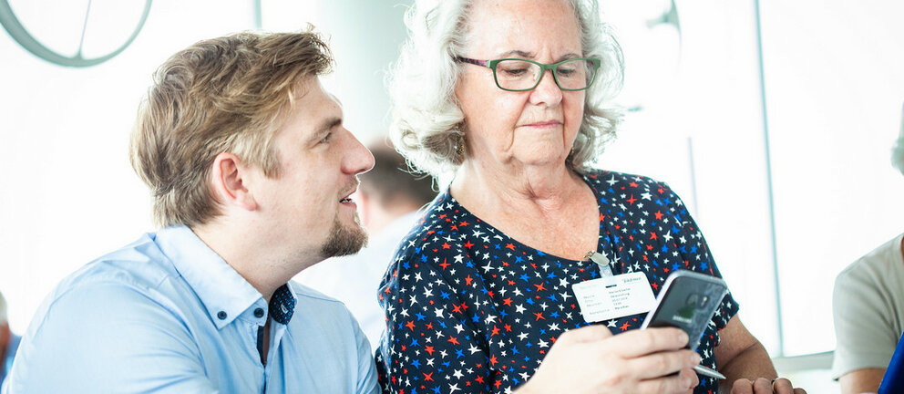 Ein Trainer erklärt einer älteren Dame etwas am Smartphone